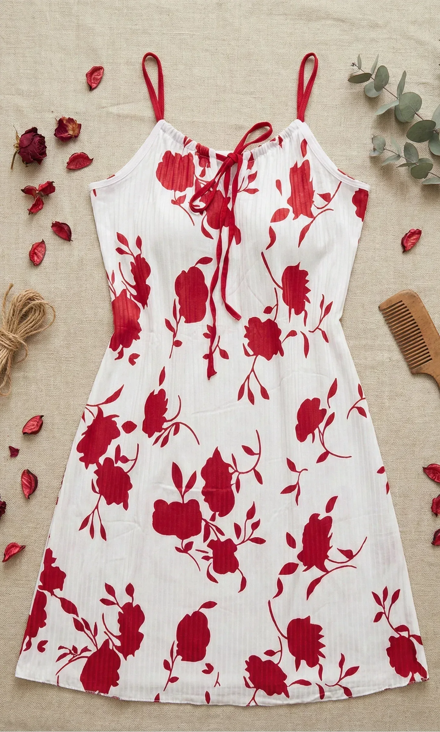 White dress with red floral pattern on a beige surface with dried flowers and a comb.