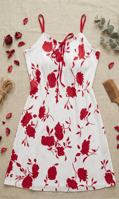 White dress with red floral pattern on a beige surface with dried flowers and a comb.